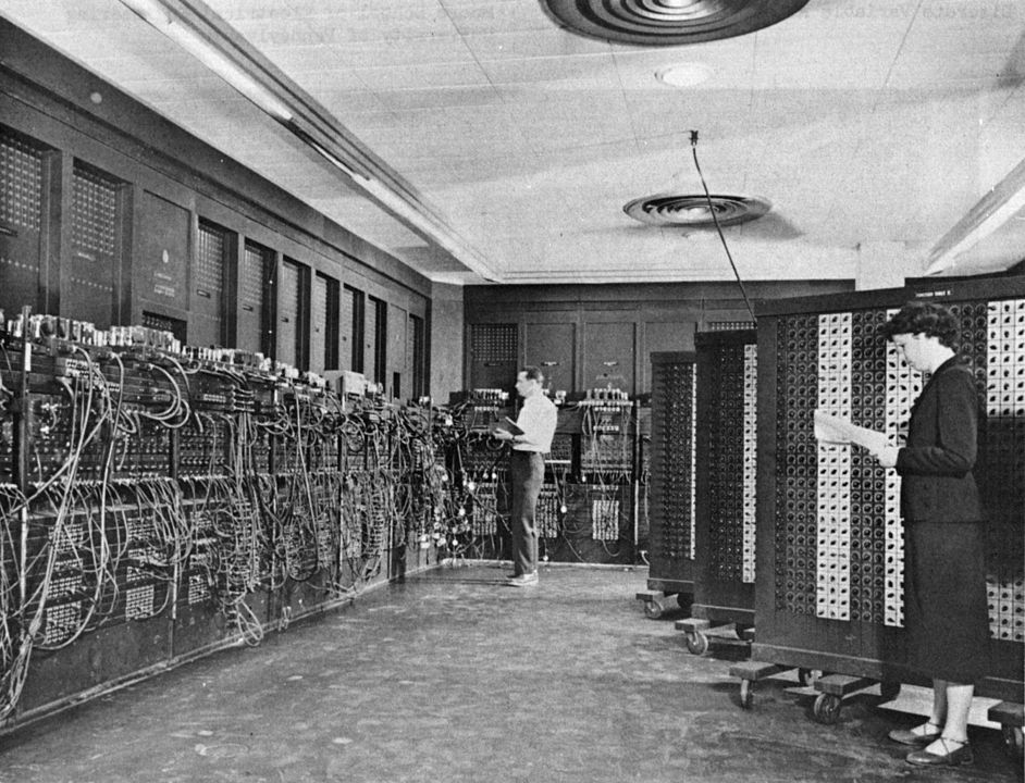 Two humans operating a computer the size of a room