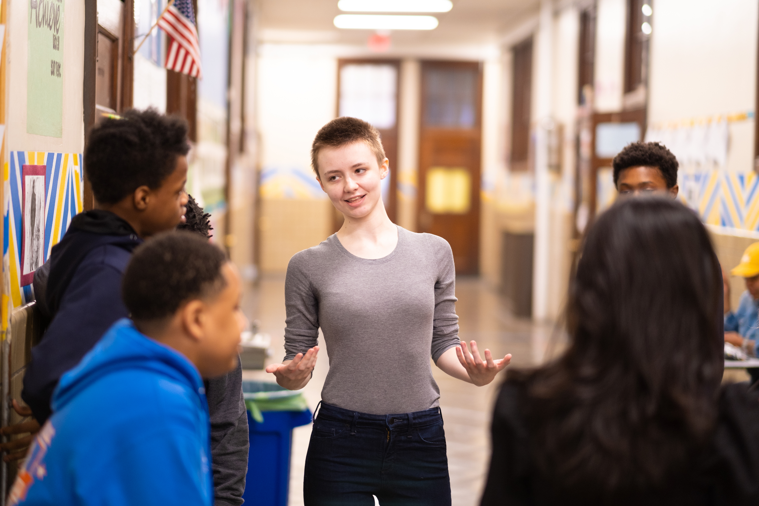 A young-adult speaks with a group of four or five young students who stand near them.