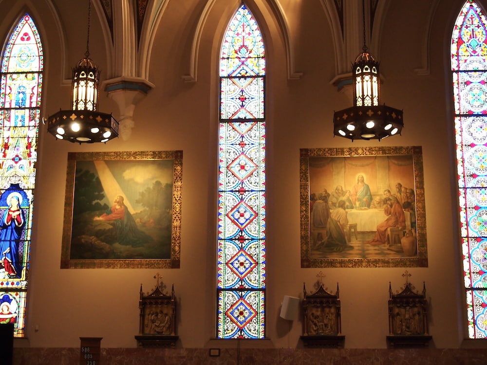Wall of a church featuring three stained glass windows and two murals on the wall