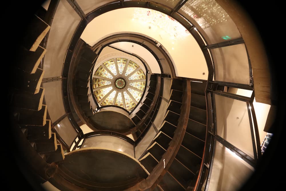 View looking up a spiral staircase to a stained glass dome