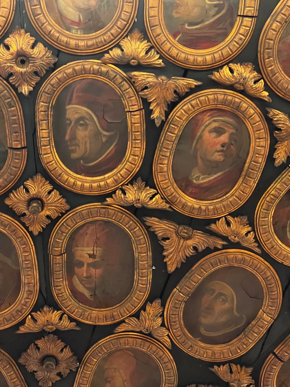 Golden frames arranged on a wall with painted Popes in Camauro caps