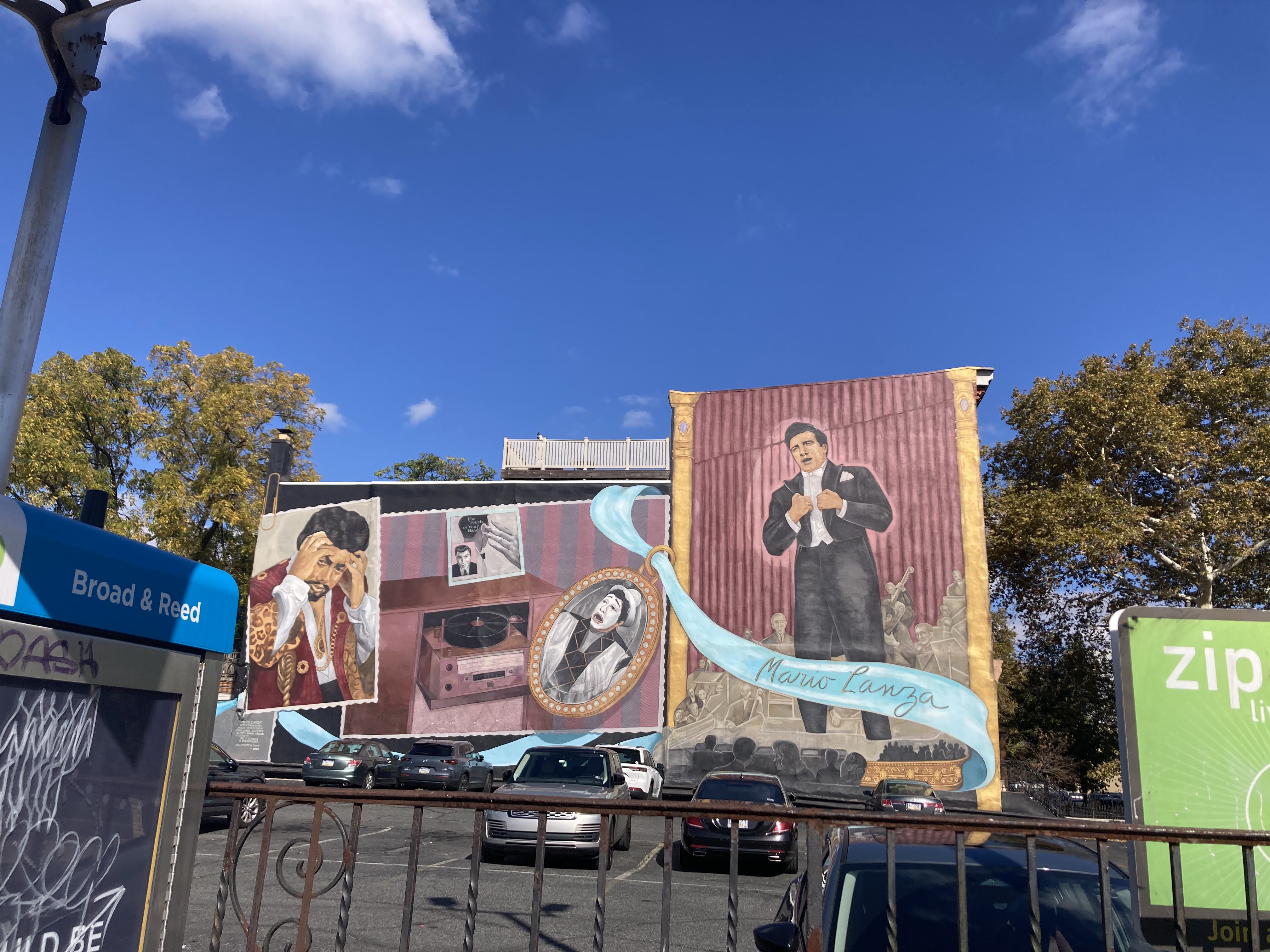 A mural depicting Mario Lanza singing. A grayscale orchestra lies behind him, and a cyan curtain drags across the foreground, featuring his name in cursive lettering.