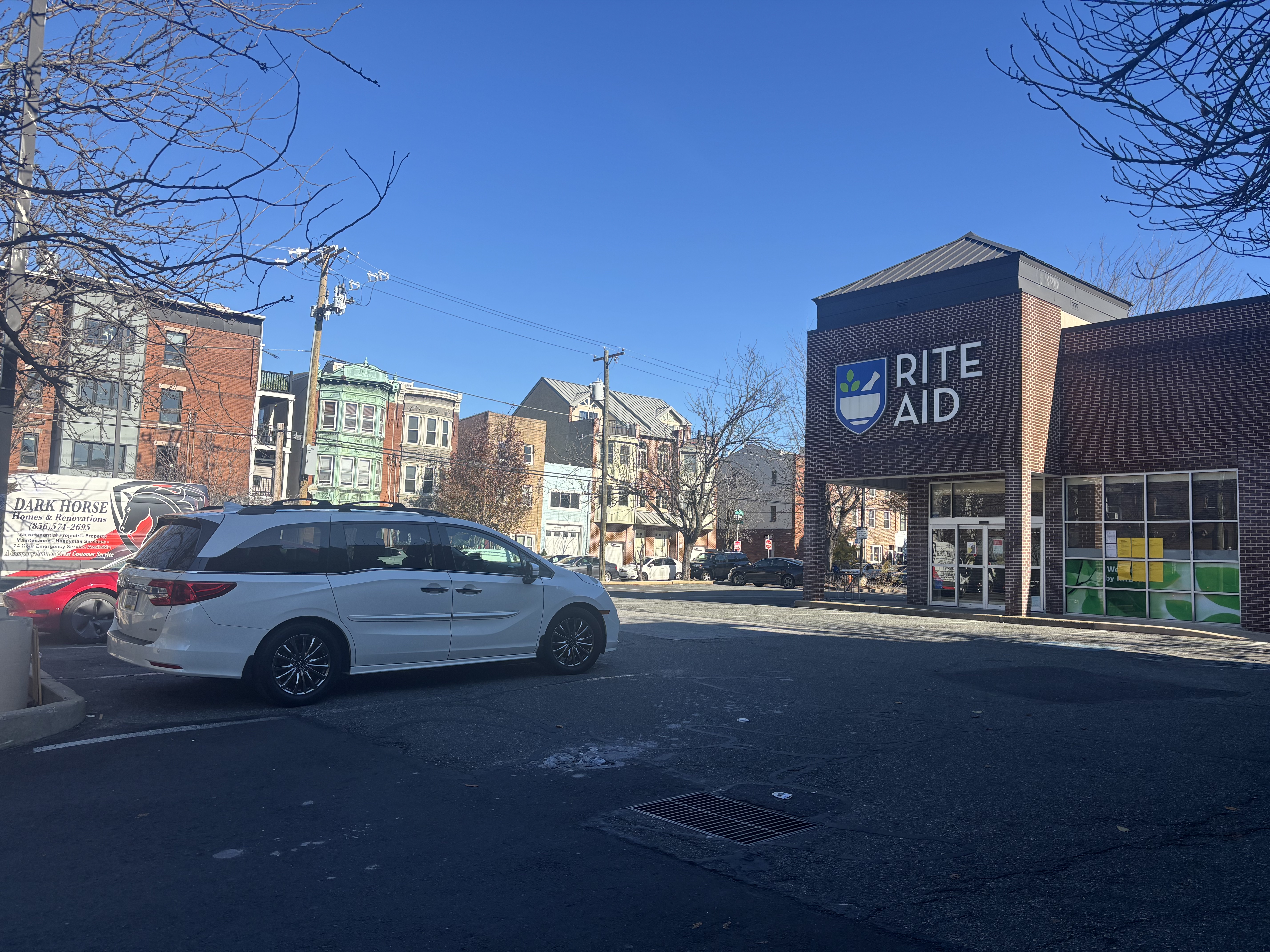 A closed Rite Aid storefront in a semi-filled parking lot in South Philadelphia. Rowhomes in the background.