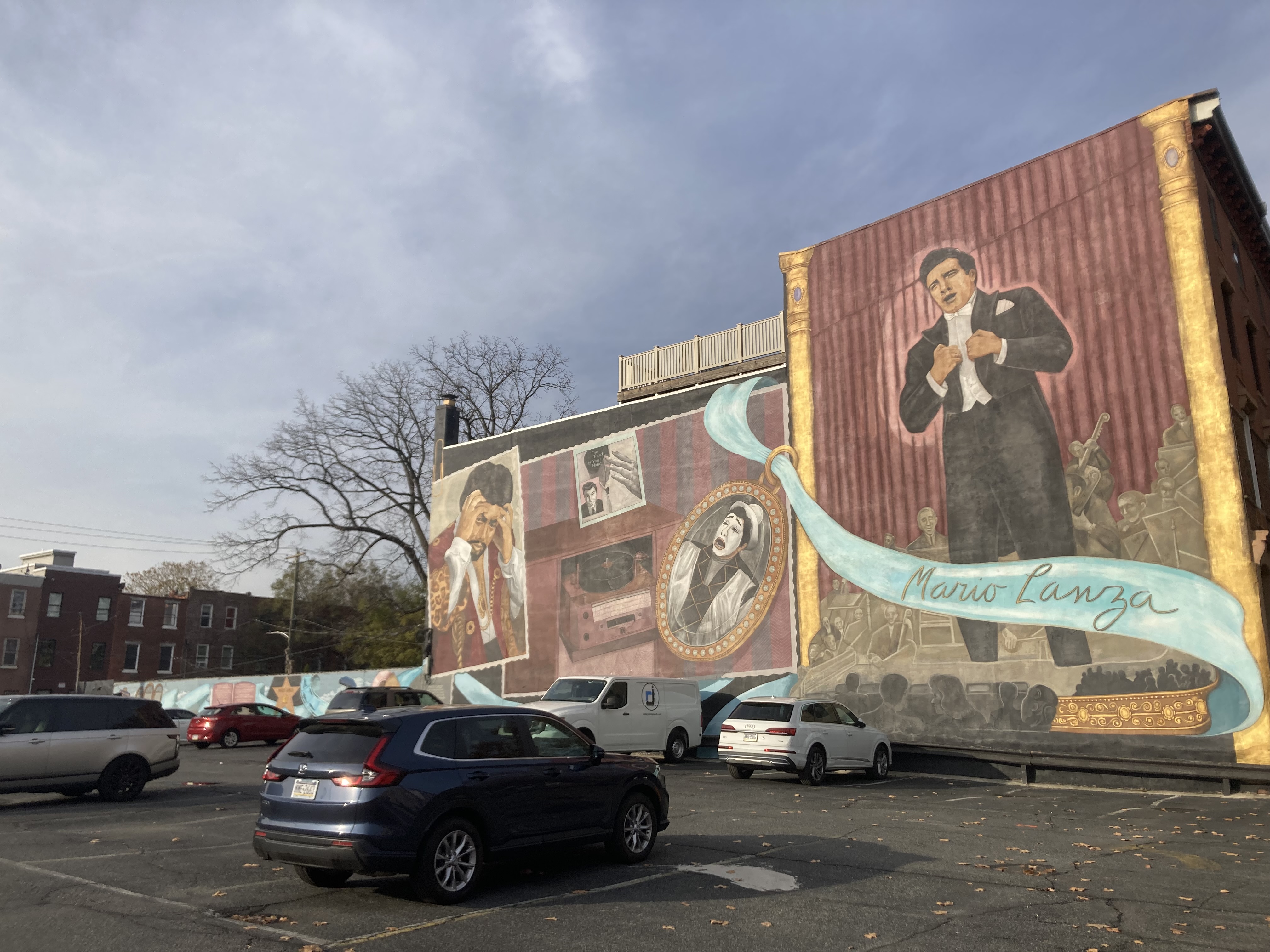 A mural depicting Mario Lanza singing. A grayscale orchestra lies behind him, and a cyan curtain drags across the foreground, featuring his name in cursive lettering.